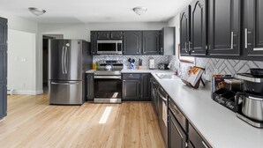 A modern kitchen with stainless steel appliances, dark cabinetry, and a herringbone tile backsplash.