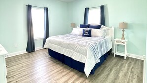Un dormitorio con cama, ventilador de techo, mesita de noche y ventana con cortinas.