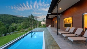 A modern outdoor pool area with a view of a forested hillside, wooden deck, and lounge chairs. - Asheville Meadows Pool, Hot Tub & Forest Views (Asheville)