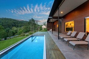 A modern outdoor pool area with a view of a forested hillside, wooden deck, and lounge chairs. - Asheville Meadows Pool, Hot Tub & Forest Views (Asheville)