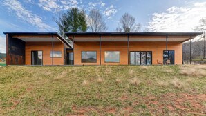 A modern two-story house with a flat roof, large windows, and a grassy hill in the foreground. - Asheville Meadows Pool, Hot Tub & Forest Views (Asheville)