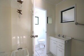 A bathroom with a toilet, sink, and a mirror on the wall. - 'The Bach'  Relaxed Holiday Accommodation Kaimaumau (Kaimaumau)