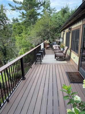 A wooden deck with outdoor furniture, a railing, and a view of trees. - Stream....Firepit....Downtown Blowing Rock.  Newly renovated. Cozy!!! (Blowing Rock)