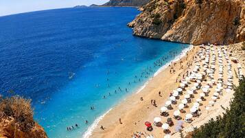 Una spiaggia con numerosi lettini e ombrelloni, una costa rocciosa e acque blu cristalline.