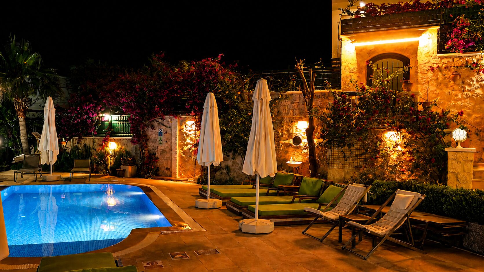 Un espace piscine nocturne avec des chaises longues et des parasols.