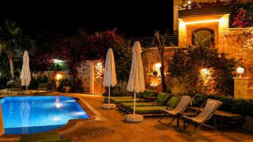 Un espace piscine nocturne avec des chaises longues et des parasols.