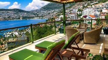 Una terrazza con mobili da esterno, vista su una cittadina costiera e una montagna sullo sfondo.
