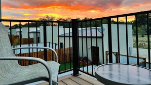 Ein Balkon mit Blick auf einen Sonnenuntergang, ein Holzzaun und ein Gebäude im Hintergrund.