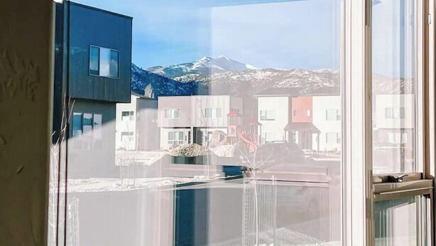 Ein modernes Gebäude mit einem großen Fenster, das einen verschneiten Berg und andere Bauten reflektiert.