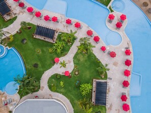 A pool area with multiple red umbrellas, lounge chairs, and a well-maintained lawn.