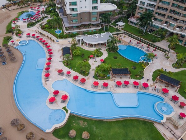 A resort with a large swimming pool, sun loungers, and a beach area.
