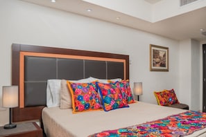 A hotel room with a large bed, two bedside lamps, a headboard, and a framed picture on the wall.