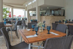 An outdoor dining area with wicker chairs and tables, blue glassware, and a kitchen in the background.