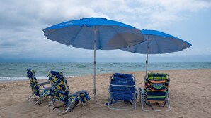 Dos sillas de playa bajo un paraguas azul en una playa arenosa, con el océano al fondo.
