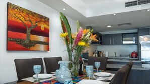 Un comedor con una mesa dispuesta para dos, un jarrón con flores y un cuadro de un árbol en la pared.