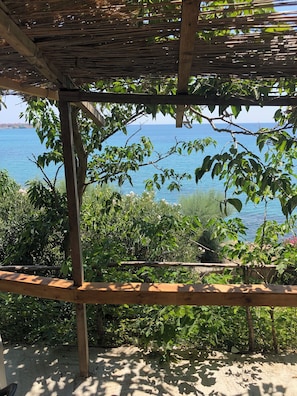 Relax in a serene outdoor space with a view of the lake, surrounded by lush greenery and a thatched roof.