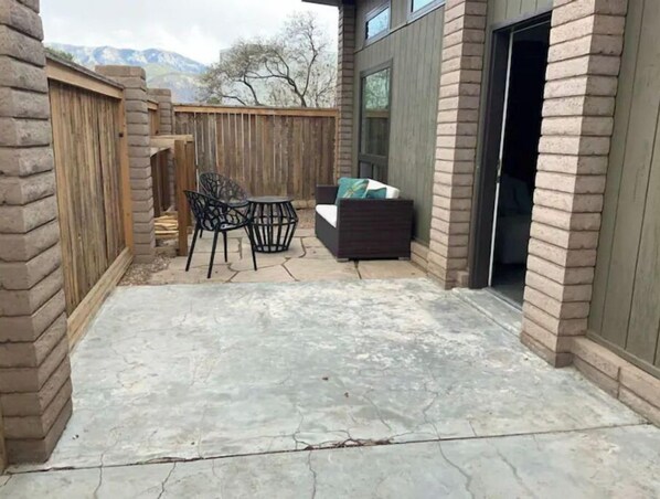 Relax on the covered patio with a sofa and chair, surrounded by a brick wall and wooden fence.