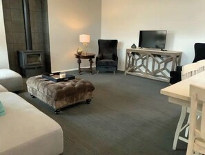Relax in this stylish living room with a plush ottoman, dark armchair, and white sofa.