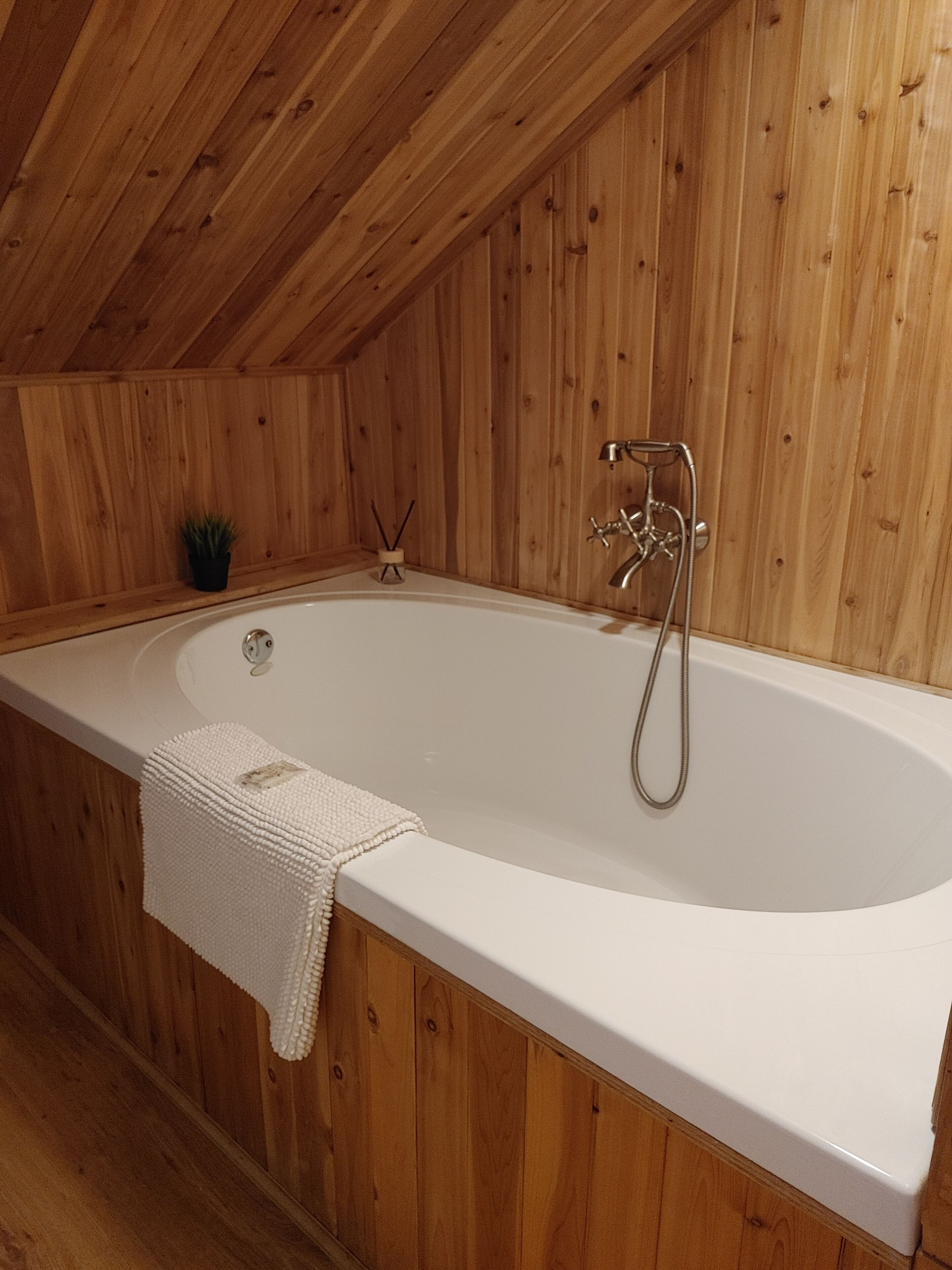 A wooden-paneled room with a white bathtub, a towel, and a small plant.