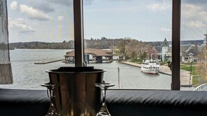 A room with a view of a lake, a boat, and buildings across the water. - Stonewater Manor (Gananoque)