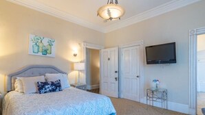 Un dormitorio con una cama grande, un televisor montado en la pared y una puerta que da a otra habitación.