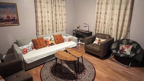 En stue med sofa, lænestol, sofabord og et tæppe. Der er et skrivebord med lampe og stol.