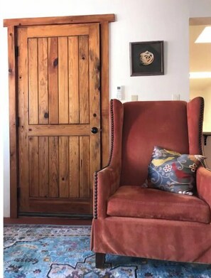 Ein Zimmer mit Holztür, einem rot gepolsterten Sessel, einem bunten Kissen und einem gemusterten Teppich.