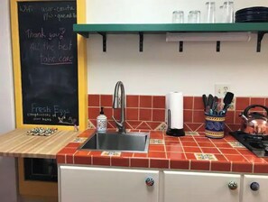 Eine Küche mit roter Fliesenrückwand, einem Edelstahlspülbecken und einer Kreidetafel mit handgeschriebenen Notizen.