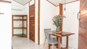 Uma área de refeições com mesa e cadeiras de madeira, um vaso com flores e uma lâmpada pendente.