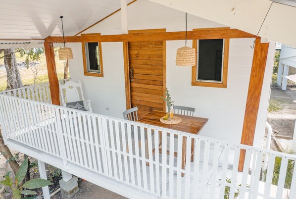 Un espace extérieur abrité, avec une table et des chaises en bois, une clôture blanche et des lampes suspendues.
