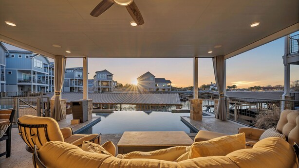 A modern outdoor lounge area with a pool, seating, and a view of the sunset over residential buildings. - Reel Oasis, family-friendly, pet friendly, pool, boat slip, golf and on lake LBJ (Kingsland)