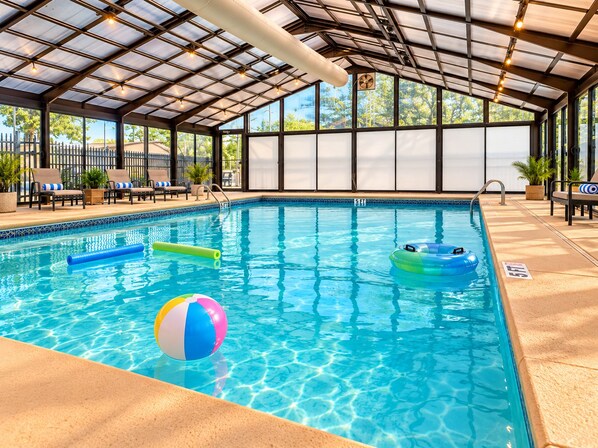An indoor swimming pool with clear water, lounge chairs, and a covered roof structure.
