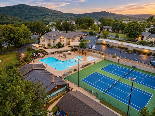 A residential area with a swimming pool, tennis courts, and a large house with a driveway.