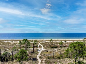 A coastal landscape with a clear sky, a sandy beach, and a narrow path leading towards the sea. - 1 min walk to Pool/ 5 min walk to BEACH /LG PATIO/ Bikes & GOLFCART Included (Port St. Joe)