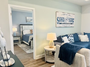 A bedroom with a bed, bedside table, lamp, and a wall sign. - 1 min walk to Pool/ 5 min walk to BEACH /LG PATIO/ Bikes & GOLFCART Included (Port St. Joe)