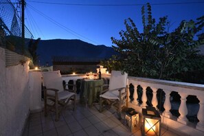 An outdoor patio with a table and chairs, a lantern, and a view of a mountain at dusk.