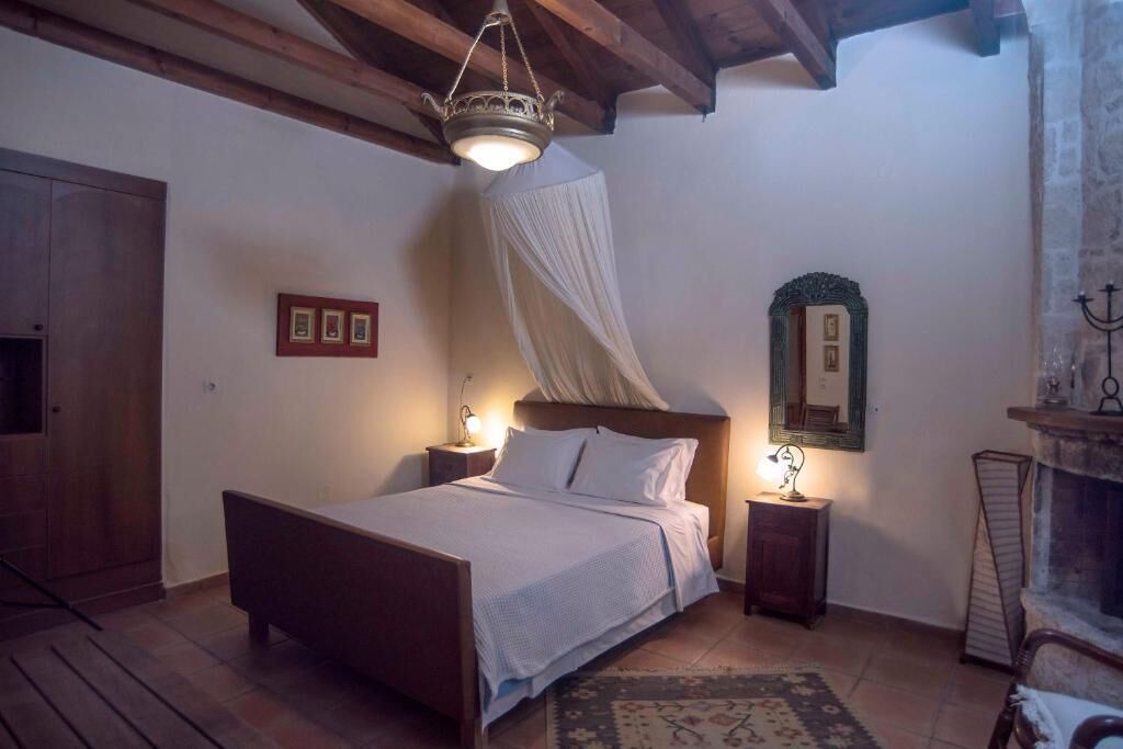 A bedroom with a wooden bed, a nightstand, a bedside lamp, a canopy bed, a mirror, and a fireplace.