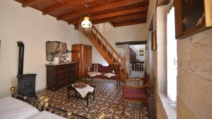 A rustic room with a wooden ceiling, a staircase, a bed, a dresser, a chair, and a table. - Troullos Traditional Houses (Archanes-Asterousia)