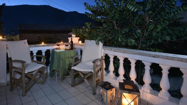 An outdoor terrace with two wooden chairs, a table with a green tablecloth, and candles. - Troullos Traditional Houses (Archanes-Asterousia)