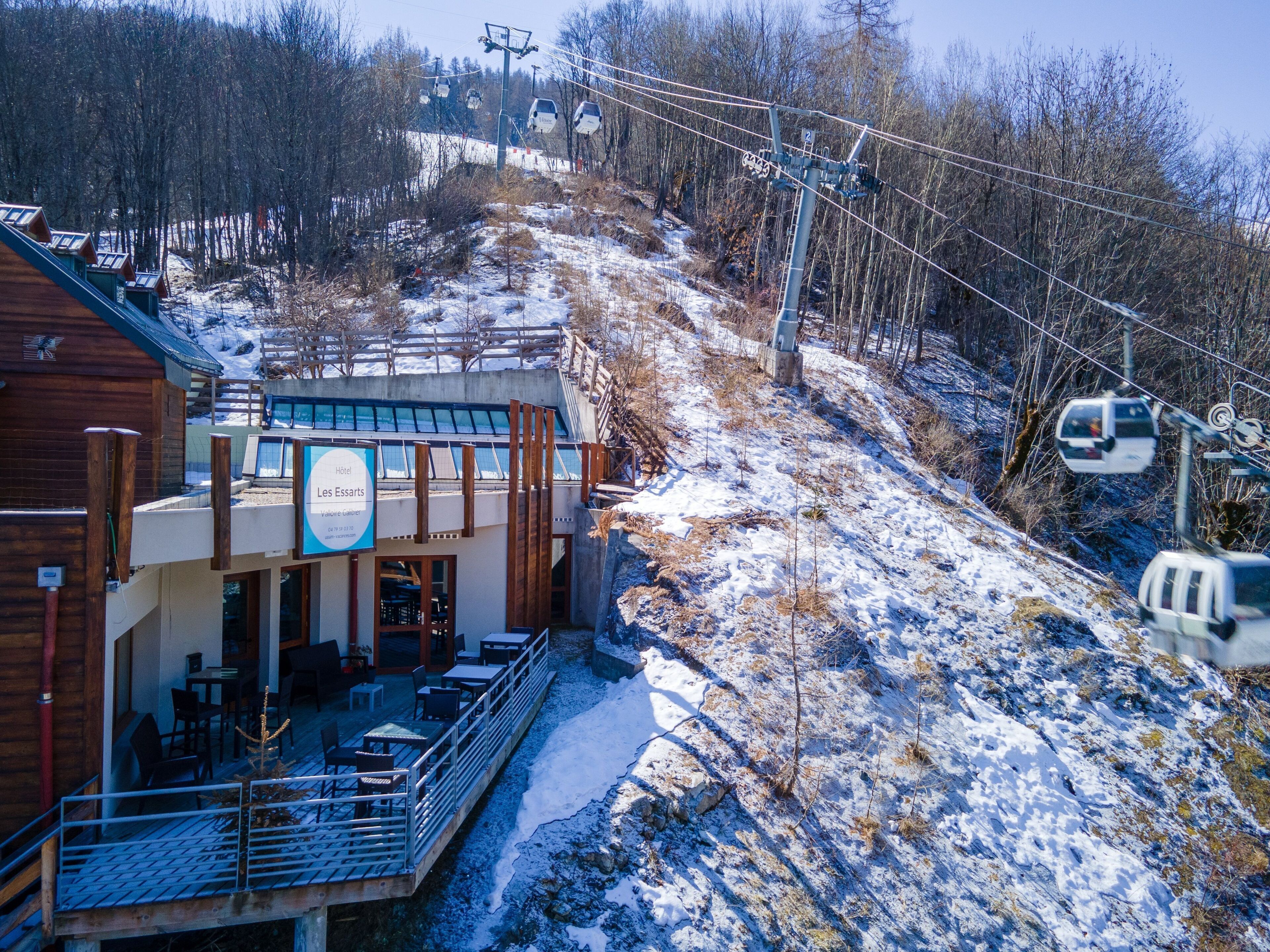 A hotel with a terrace, outdoor seating, and a ski lift in the background.