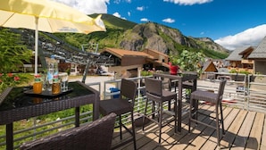 Une terrasse extérieure avec des meubles en osier, un parasol jaune et une vue sur les montagnes.
