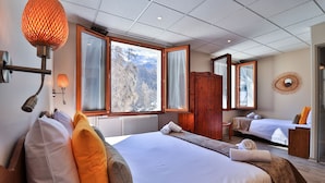 Une chambre d’hôtel avec deux lits, une grande fenêtre donnant sur les montagnes, une armoire en bois et un miroir au mur.