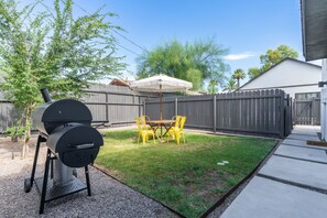 Un pati d'era amb una barbacoa, una taula amb caires grogues i un para-sol.