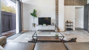 Ein modernes Wohnzimmer mit Glastisch, Ledersofas, einem Flachbildfernseher und einer Ziegelwand als Blickfang.