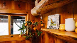 A wooden cabin interior with a potted orange tree, a rooster-themed picture frame, and a white pitcher on a shelf. - The Building on The River R&R  (Riggins)