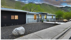 A row of cabins with a mountain backdrop, gravel ground, and a paved path. - The Building on The River R&R  (Riggins)