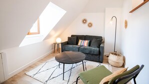 A cozy loft bedroom with a sloped ceiling, a dark grey sofa, a round coffee table, and a small side table with a lamp. - Le Quai des Marais - Coeur d'Amboise (Amboise)