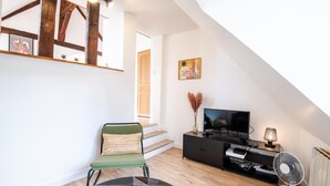 A modern living room with a high ceiling, a television, a fan, and a chair. - Le Quai des Marais - Coeur d'Amboise (Amboise)