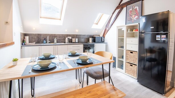A modern kitchen with a dining area, featuring a black refrigerator, wooden table, and a loft-style ceiling with exposed beams. - Le Quai des Marais - Coeur d'Amboise (Amboise)