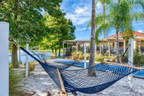 A hammock by a pool with a pergola and palm trees in the background. - Magical 7BR Resort Pool Home Near Disney World (Kissimmee)
